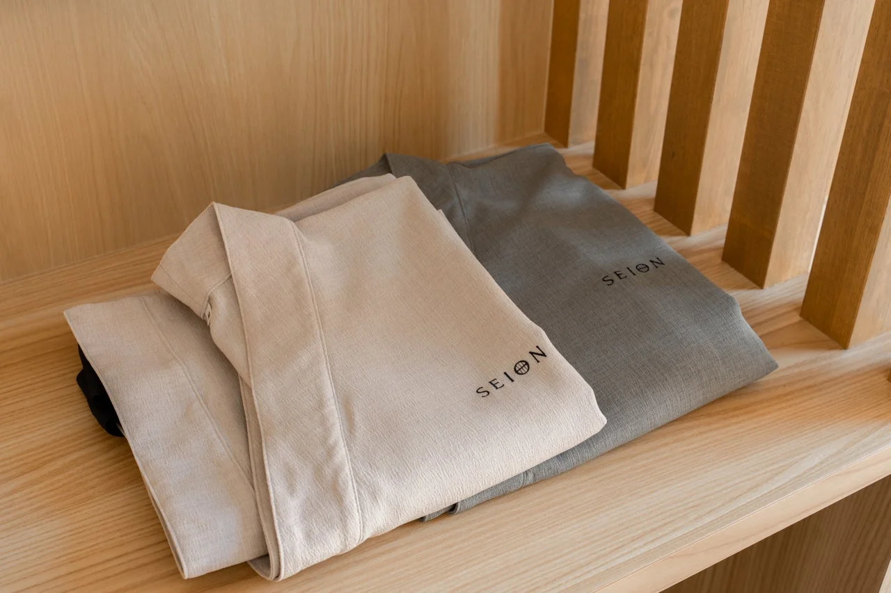 木目調の棚に、ベージュとグレーの「SEION」のロゴが入った浴衣またはバスローブが丁寧にたたんで置かれています。清潔感があり、宿泊施設の客室アメニティを思わせる落ち着いた雰囲気です。