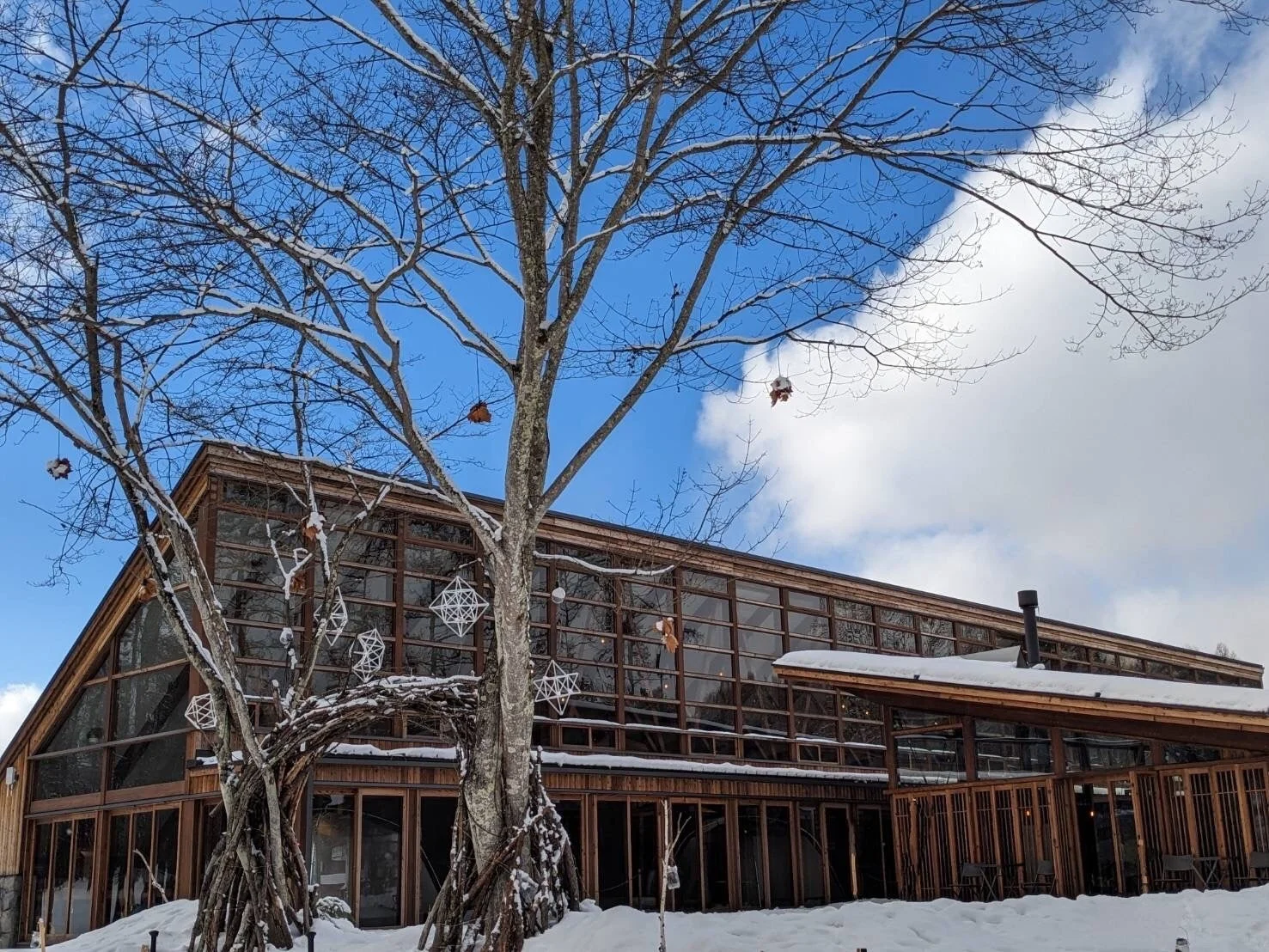 雪に覆われた地面と雪化粧した木々が手前に広がり、奥にはガラス張りのモダンな木造建築