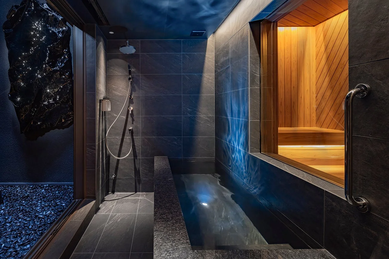 モダンでラグジュアリーなバスルーム。深めの浴槽とシャワー、そして木製のサウナが一体となった空間です。壁面には光るオブジェがあり、リラックスできる洗練された雰囲気を醸し出しています。