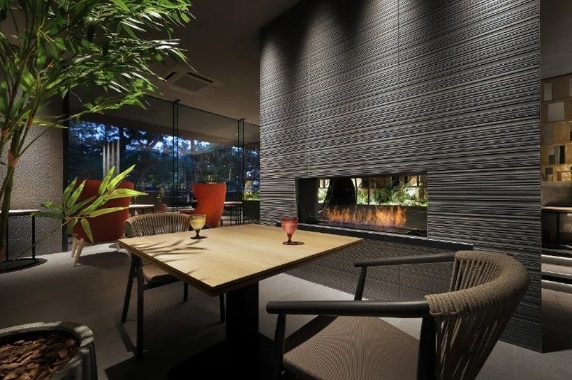 現代的で洗練された空間に、炎が揺らめく暖炉と窓外の緑が配置された豪華なインテリア