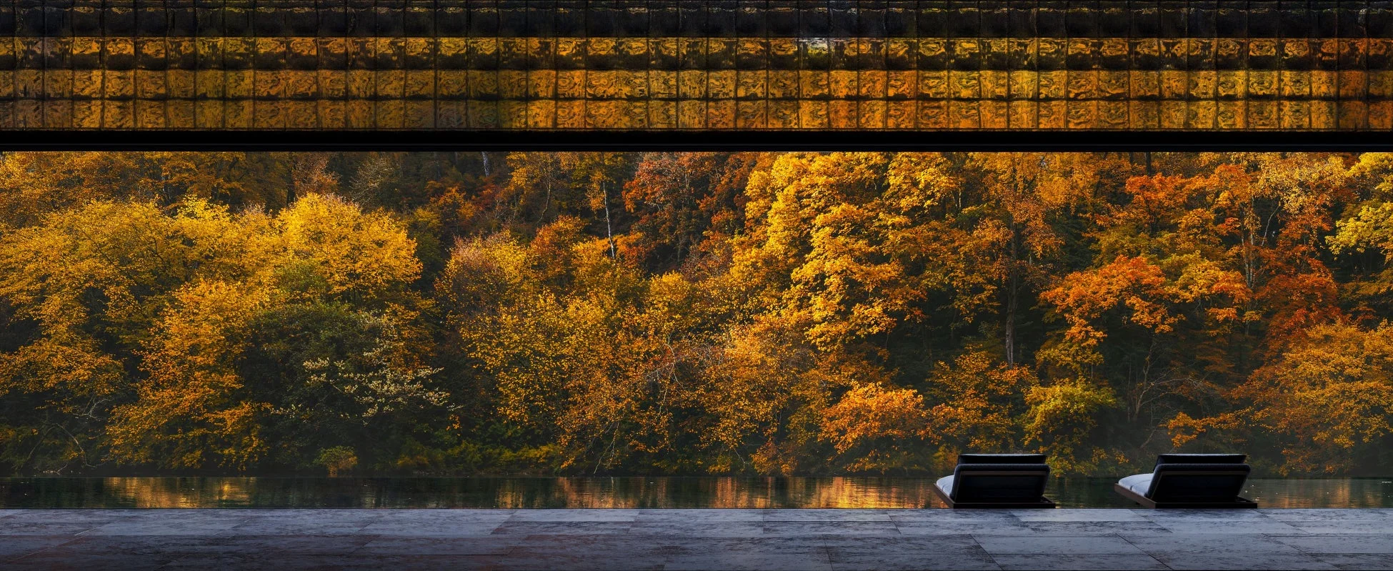 鮮やかな紅葉の森を望むインフィニティプールと、そのほとりに置かれた2脚のラウンジチェアが特徴的な、秋の美しい風景。