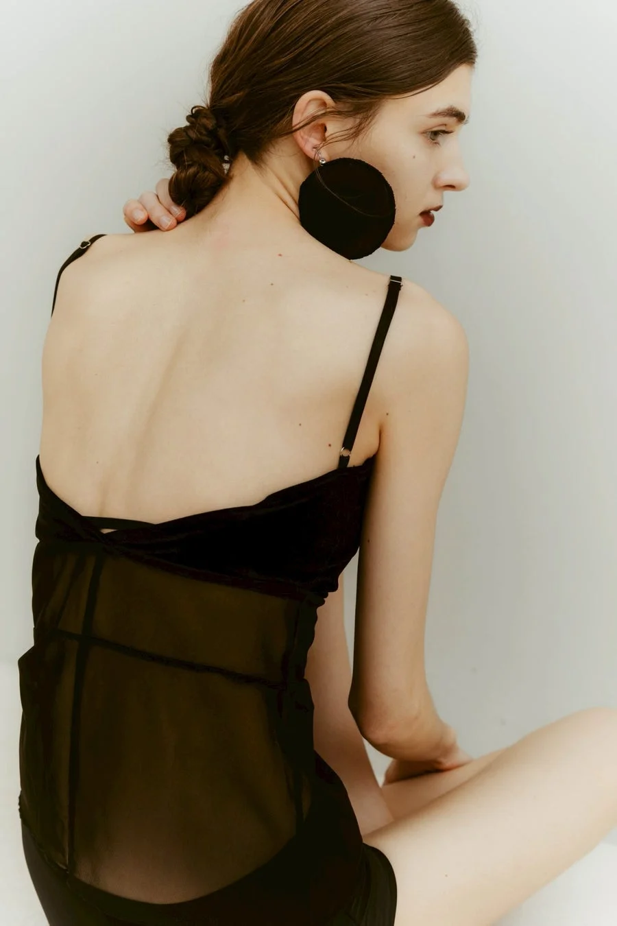 黒いシアー素材のキャミソールと大きなイヤリングをつけた女性の後ろ姿