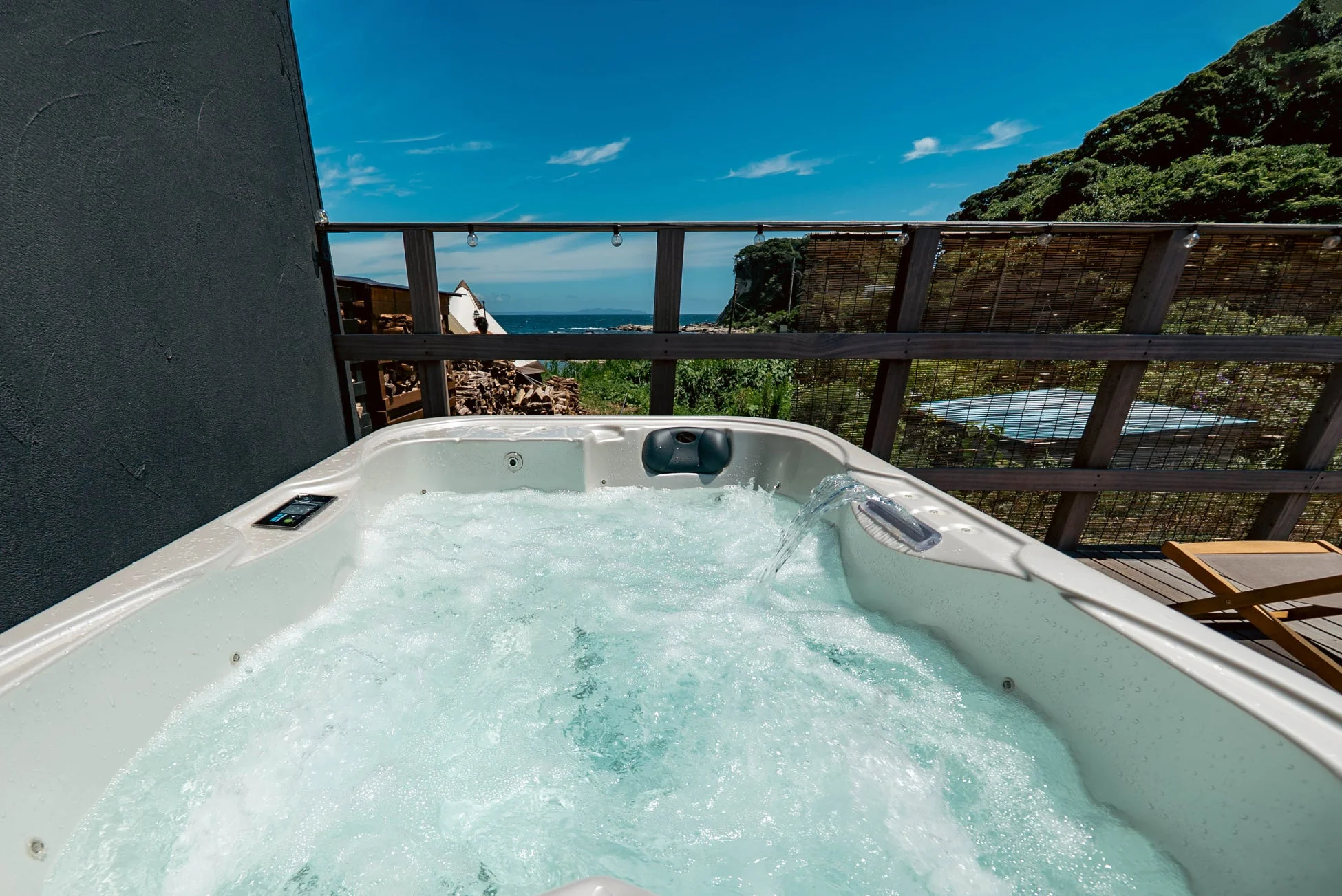 晴れた日に海と緑の景色を望むテラスに設置された、泡立つジャグジー