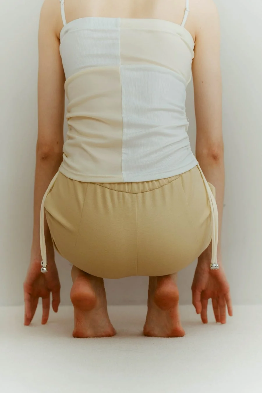 白とベージュのツートンカラーのトップスを着用し、しゃがみ込んだ人物の後ろ姿