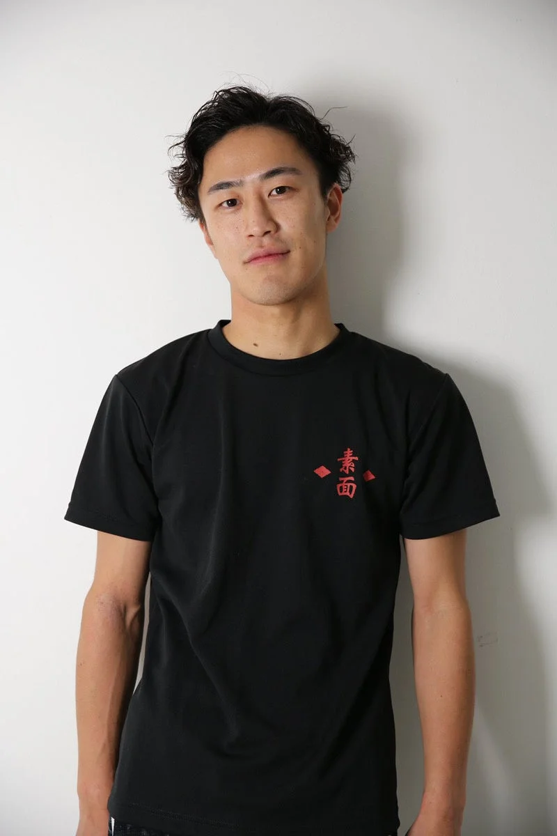 白い背景の前に立つ、黒いTシャツを着た若いアジア人男性