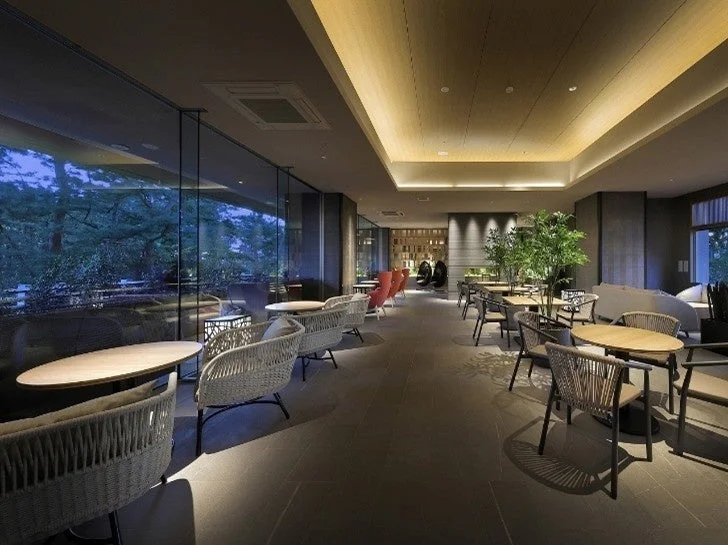 広々とした窓から緑豊かな景色を望む、モダンで洗練されたラウンジまたはカフェ空間