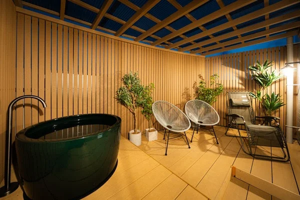 プライベートなテラスに深緑色のバスタブとスタイリッシュな椅子