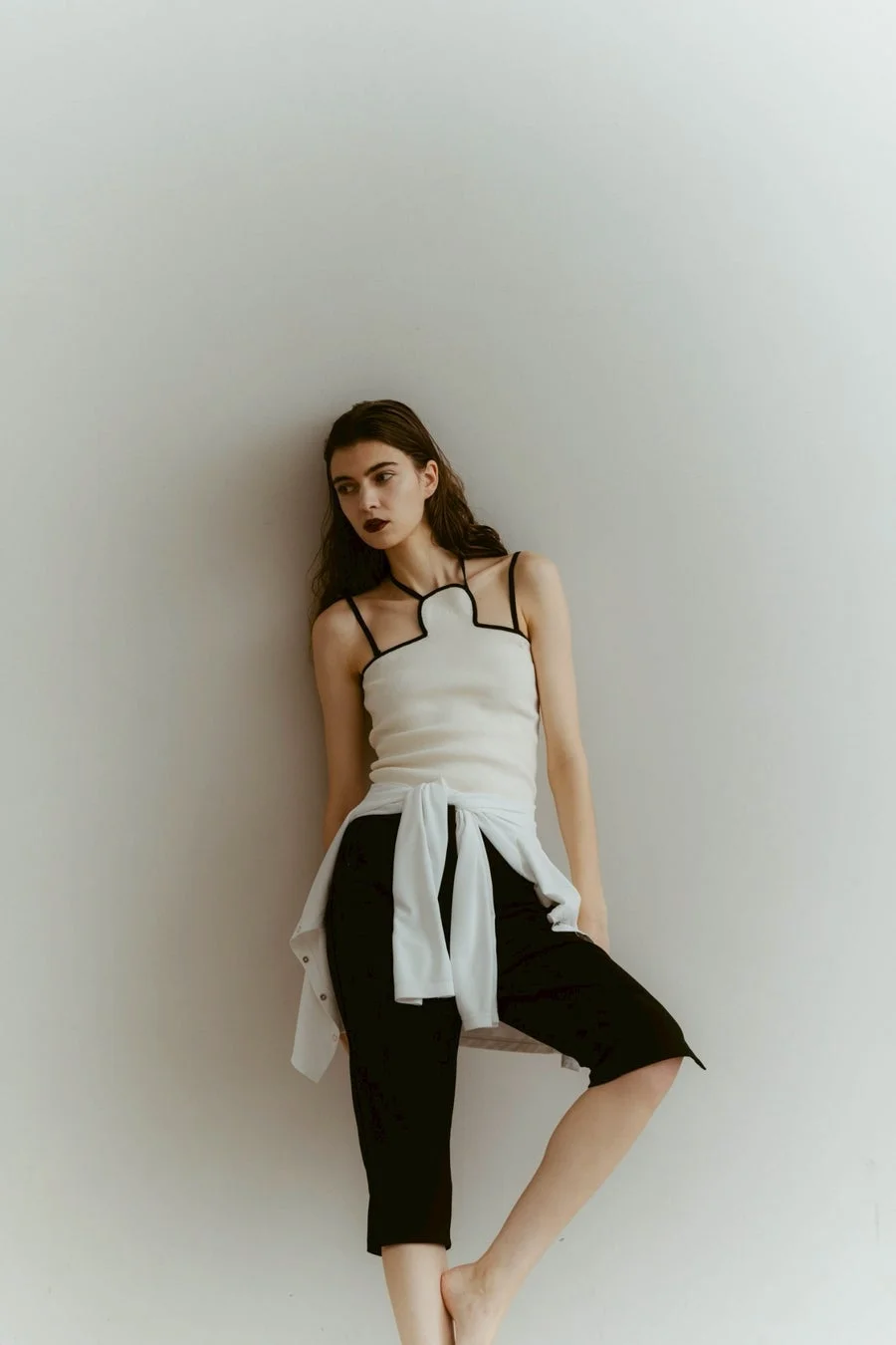 女性が白い壁にもたれかかるポートレート