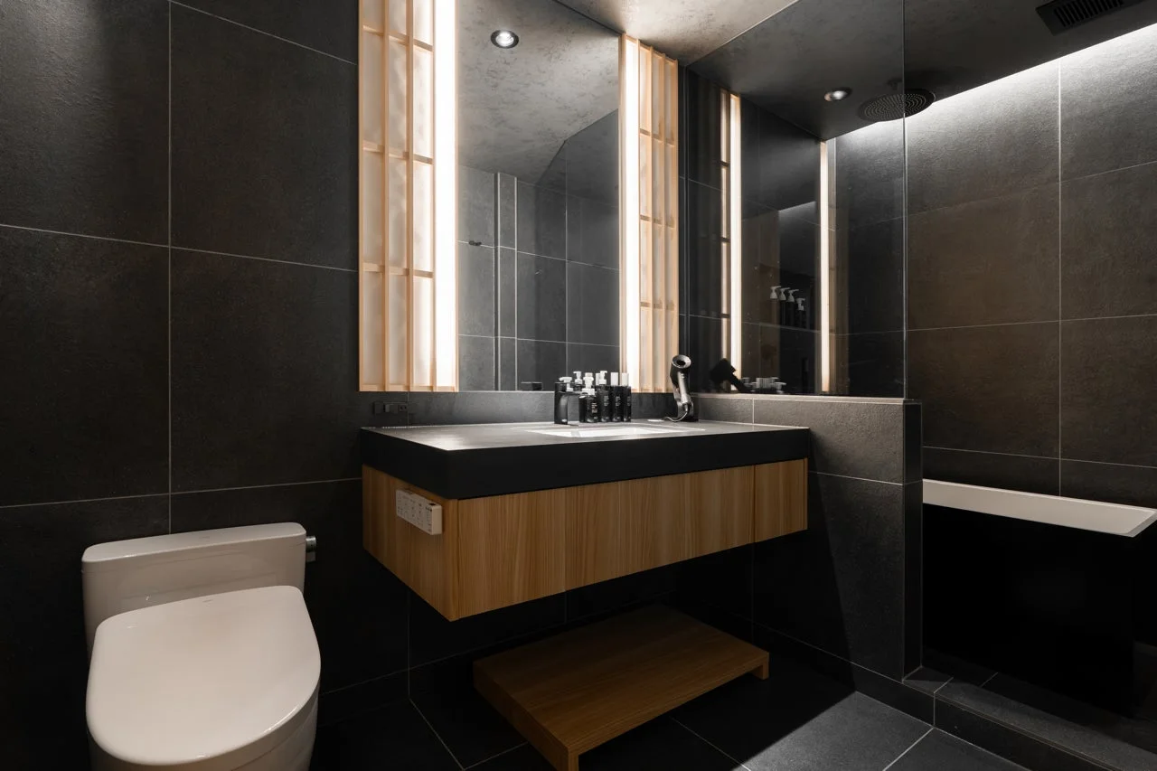 黒を基調としたモダンでスタイリッシュなバスルームです。木目調の洗面台と大きな鏡が特徴的で、シャワーとバスタブ、トイレが一体となった機能的な空間が広がっています。落ち着いた雰囲気が魅力です。