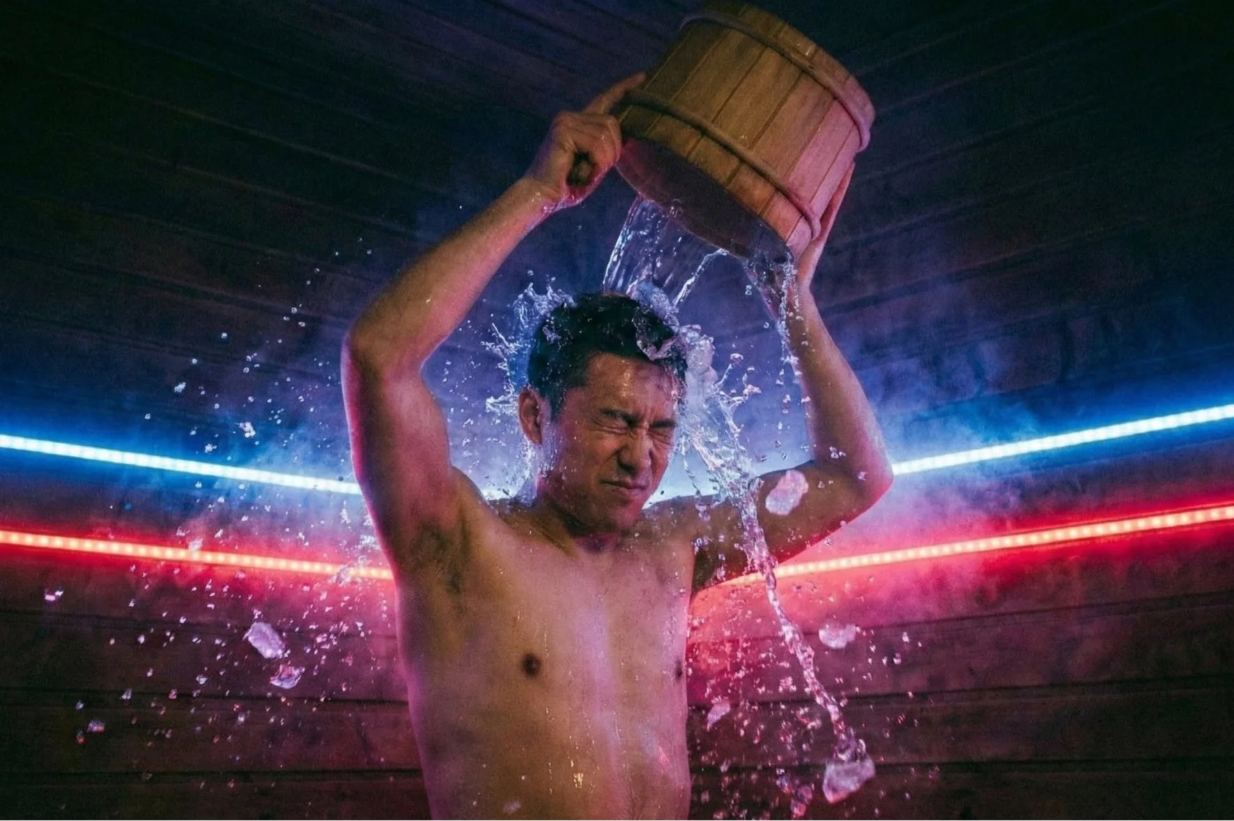 冷たい水を頭からかぶる男性の姿。水しぶきが飛び散り、顔をしかめています