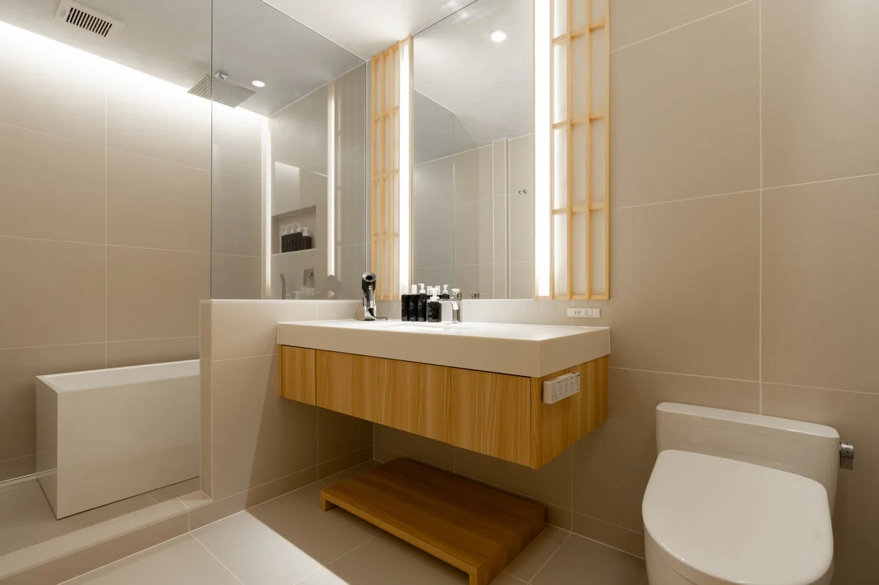 清潔感のあるモダンなバスルームで、大きな鏡のある洗面台、シャワー付きバスタブ、トイレが一体化した空間です。木目調のキャビネットと間接照明が特徴で、ホテルライクな落ち着いた雰囲気を醸し出しています。