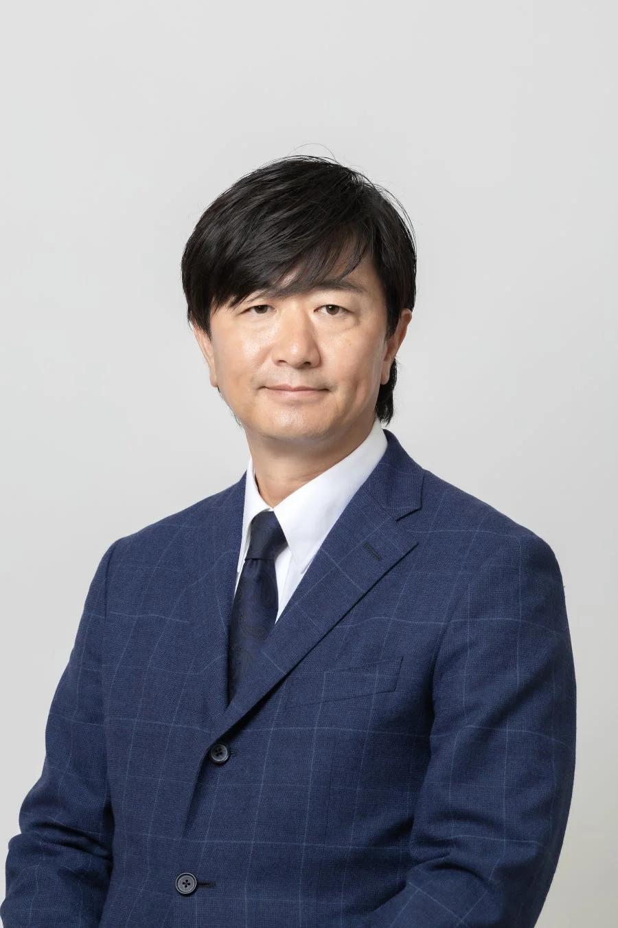 青いチェック柄のスーツとネクタイを着用したアジア人男性のポートレートです。男性はカメラをまっすぐ見ており、真面目な表情をしています。ビジネスシーンやプロフィール写真に適した画像です。