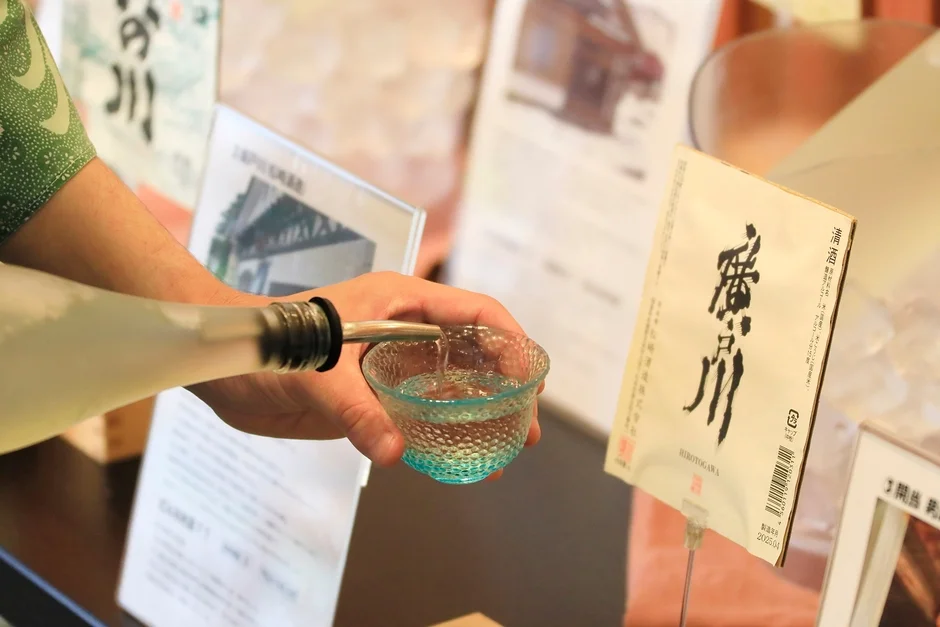 日本酒の試飲イベントで、透明なボトルから青いガラスの杯に日本酒が注がれている様子