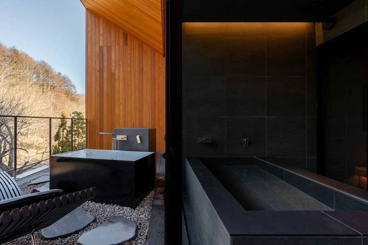 自然豊かな景色を望むテラスに露天風呂と、隣接するモダンな内風呂が写っています。木材とダークトーンの石材が調和した、落ち着いた雰囲気の高級感あふれる空間です。