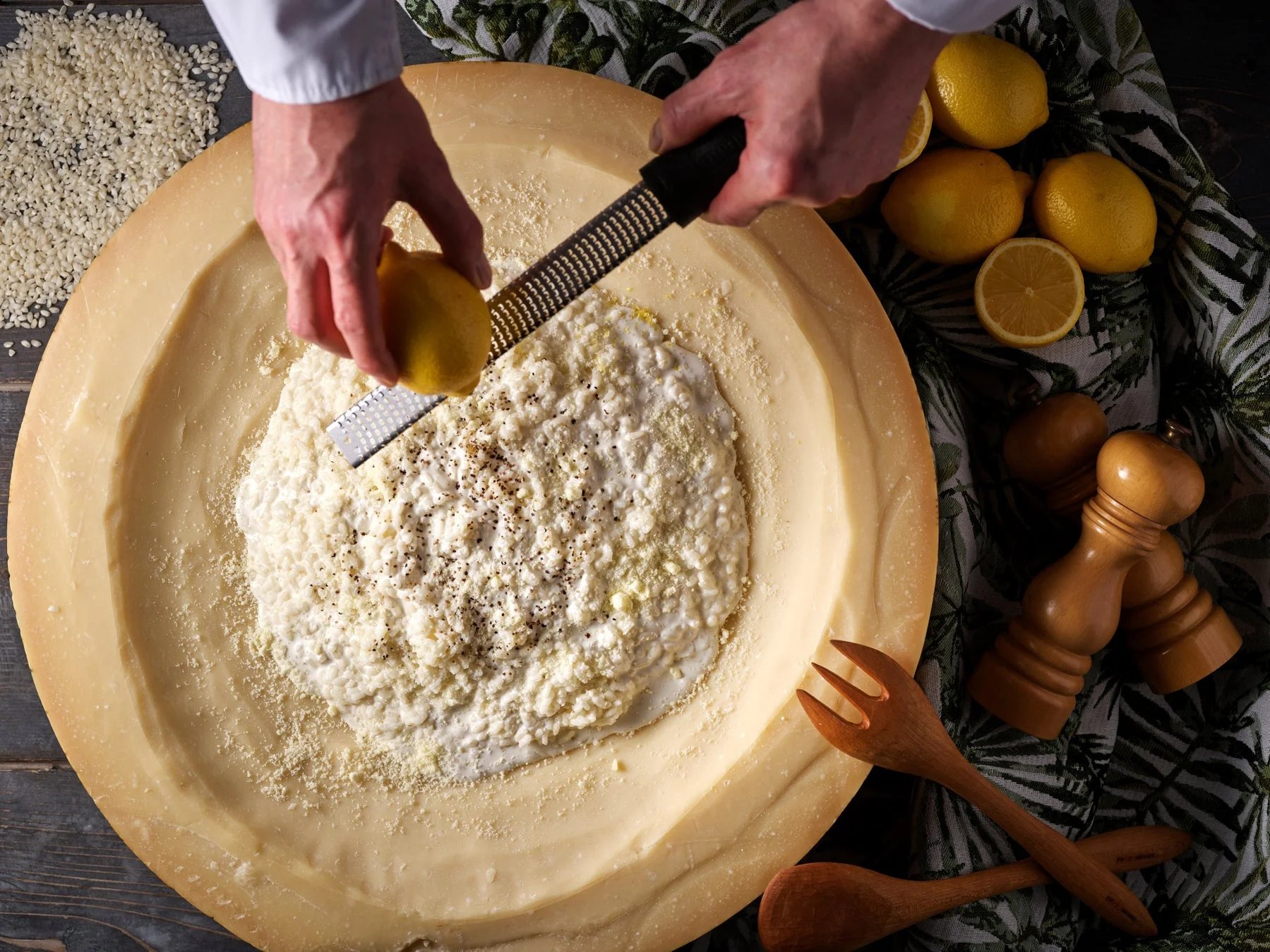 パルミジャーノチーズの大きな塊の中でレモンをすりおろして料理を仕上げる様子