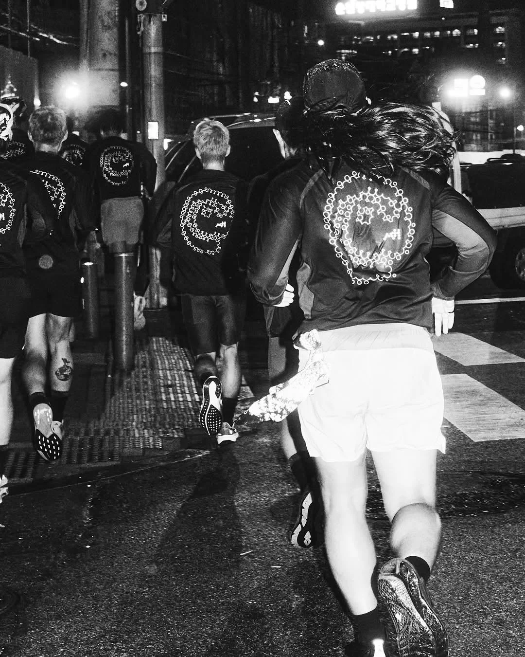 夜の街中を走る人々の後ろ姿を捉えたモノクロ写真