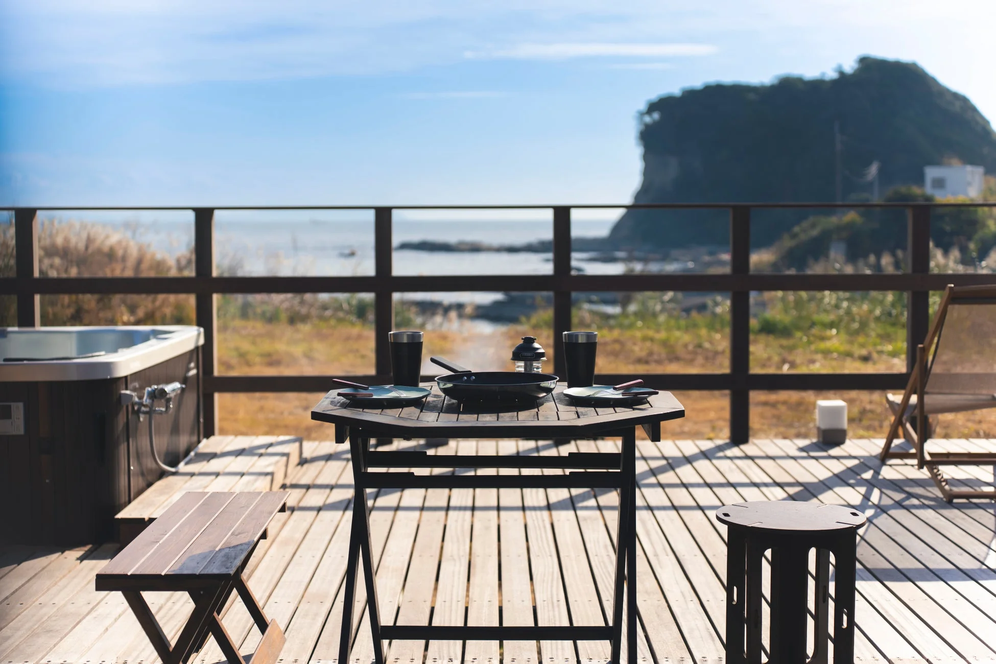 海を望む広々としたウッドデッキに、ホットタブと食事が用意されたテーブルが配置されています