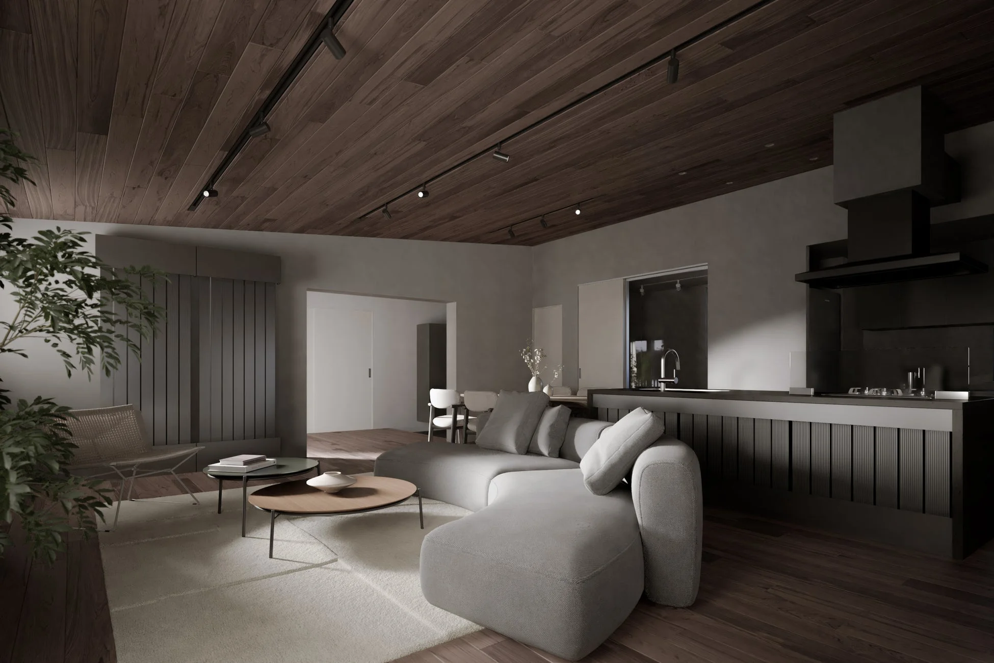 モダンで洗練されたLDK空間で、グレーのL字型ソファが特徴的です。ダークトーンのウッドパネルの天井と床、そしてグレーの壁が落ち着いた雰囲気を醸し出し、観葉植物がアクセントになっています。オープンなキッチンエリアも備わっています。