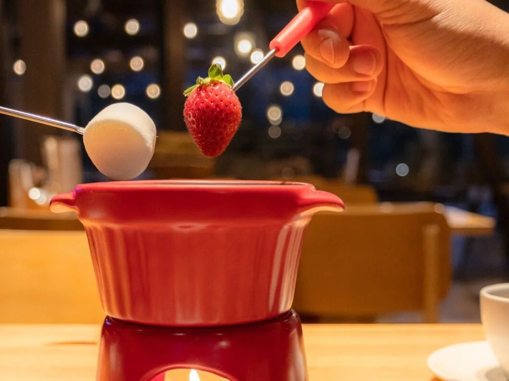 赤いフォンデュ鍋で、いちごやマシュマロをチョコレートに浸そうとしている様子