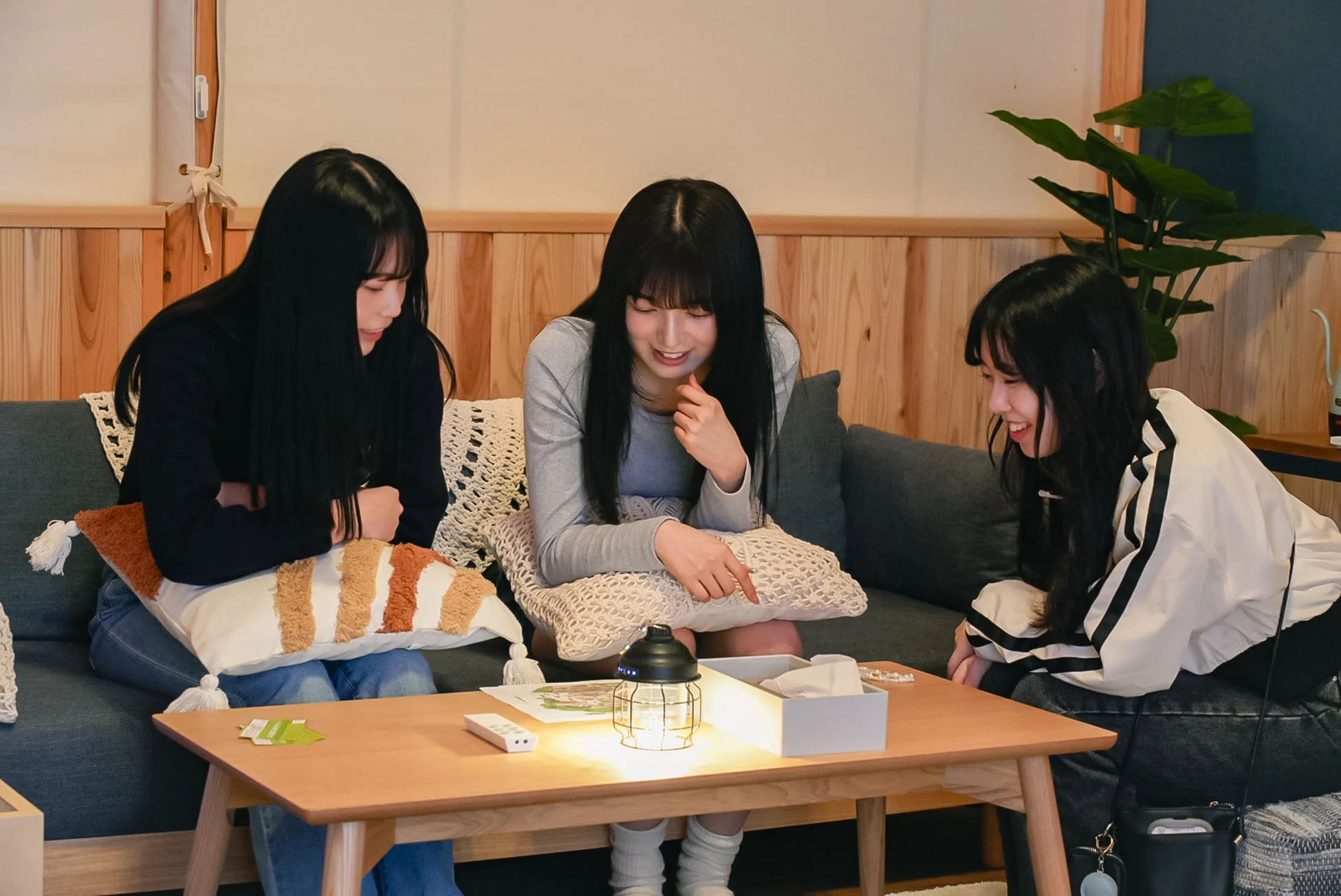 居心地の良い室内で、3人の若い女性がソファに座り、木製テーブルを囲んで談笑している様子